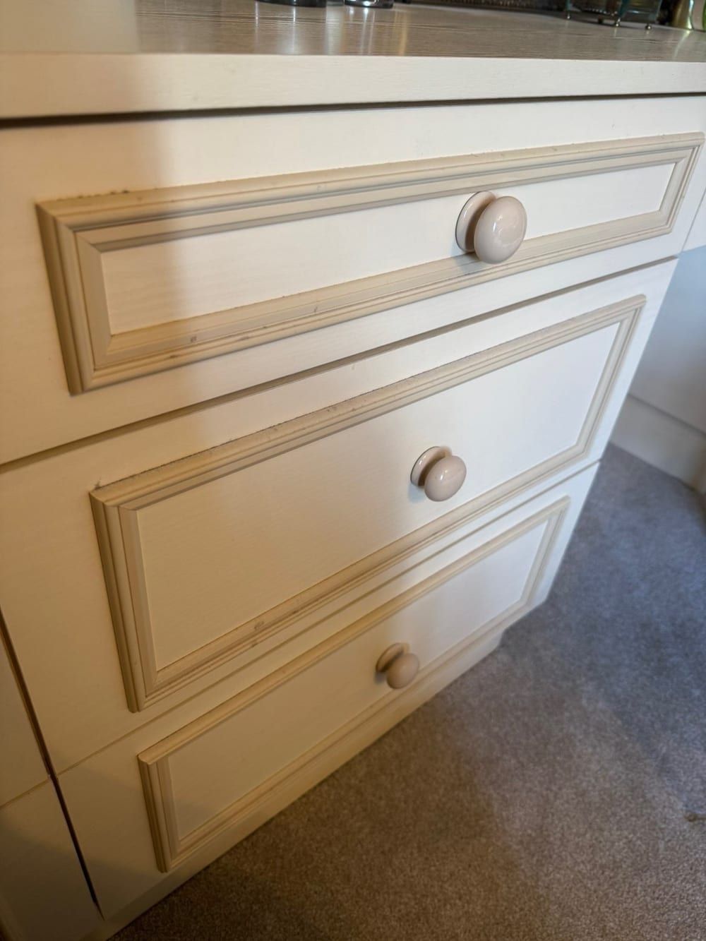 Before cleaning: cream panelled bedroom drawers with ceramic knobs