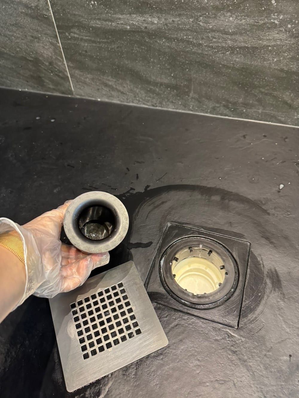 After cleaning: shower drain trap lifted out of a black shower tray