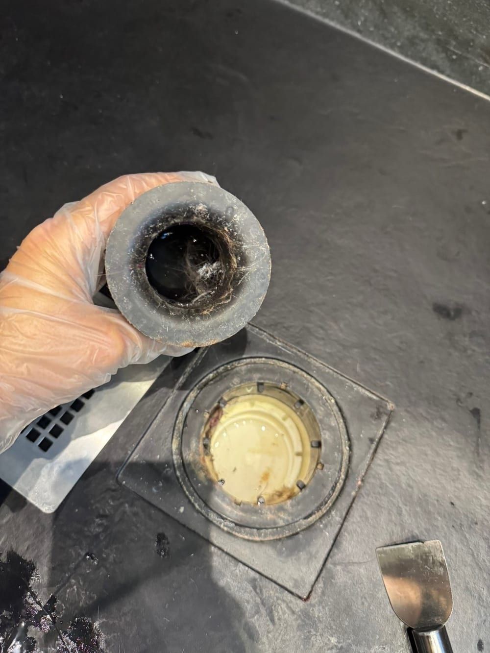 Before cleaning: shower drain trap lifted out of a black shower tray