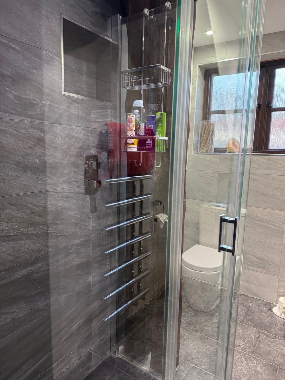 After cleaning: glass shower screen and chrome towel rail in a grey tiled shower room