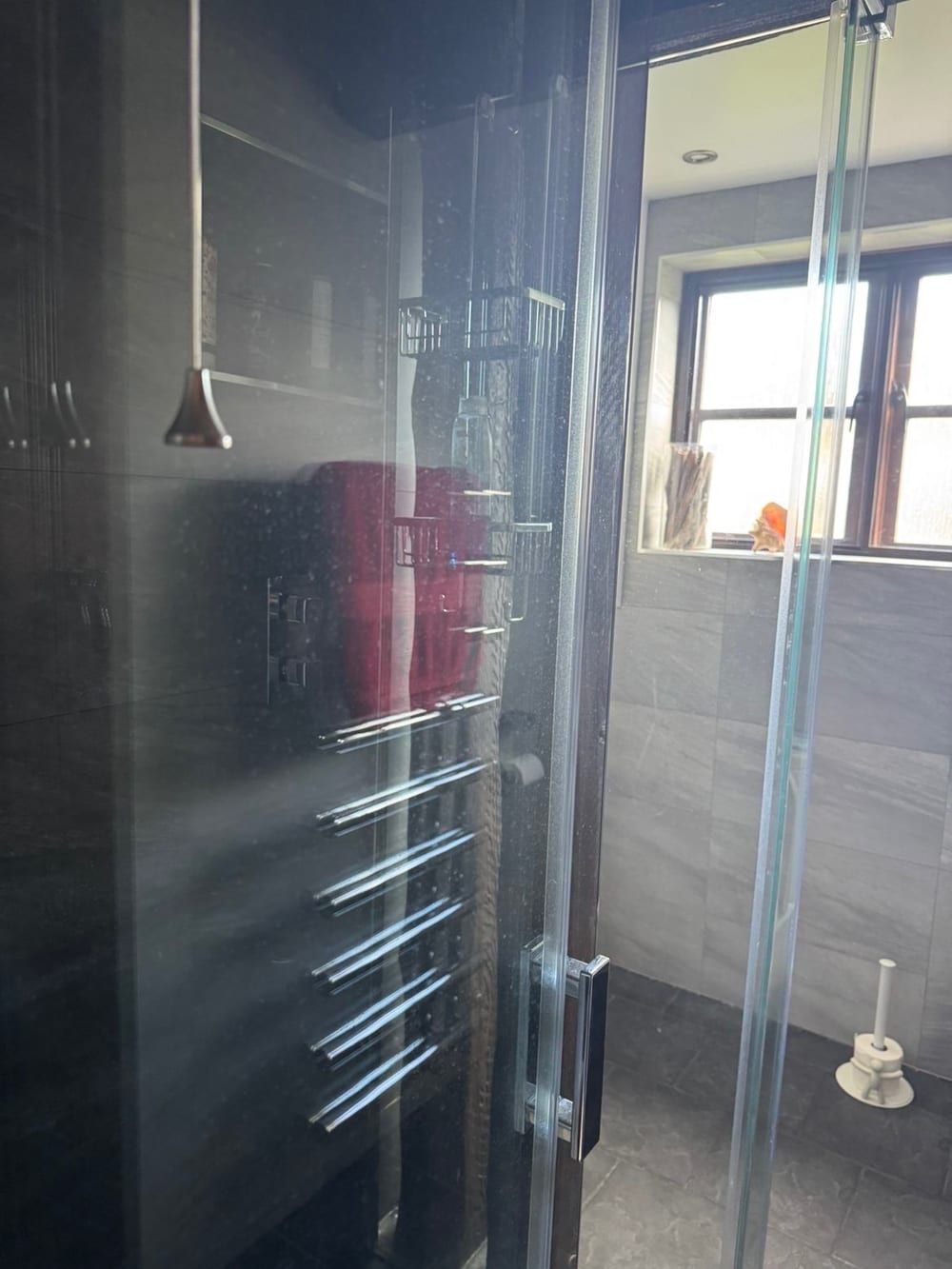 Before cleaning: glass shower screen and chrome towel rail in a grey tiled shower room